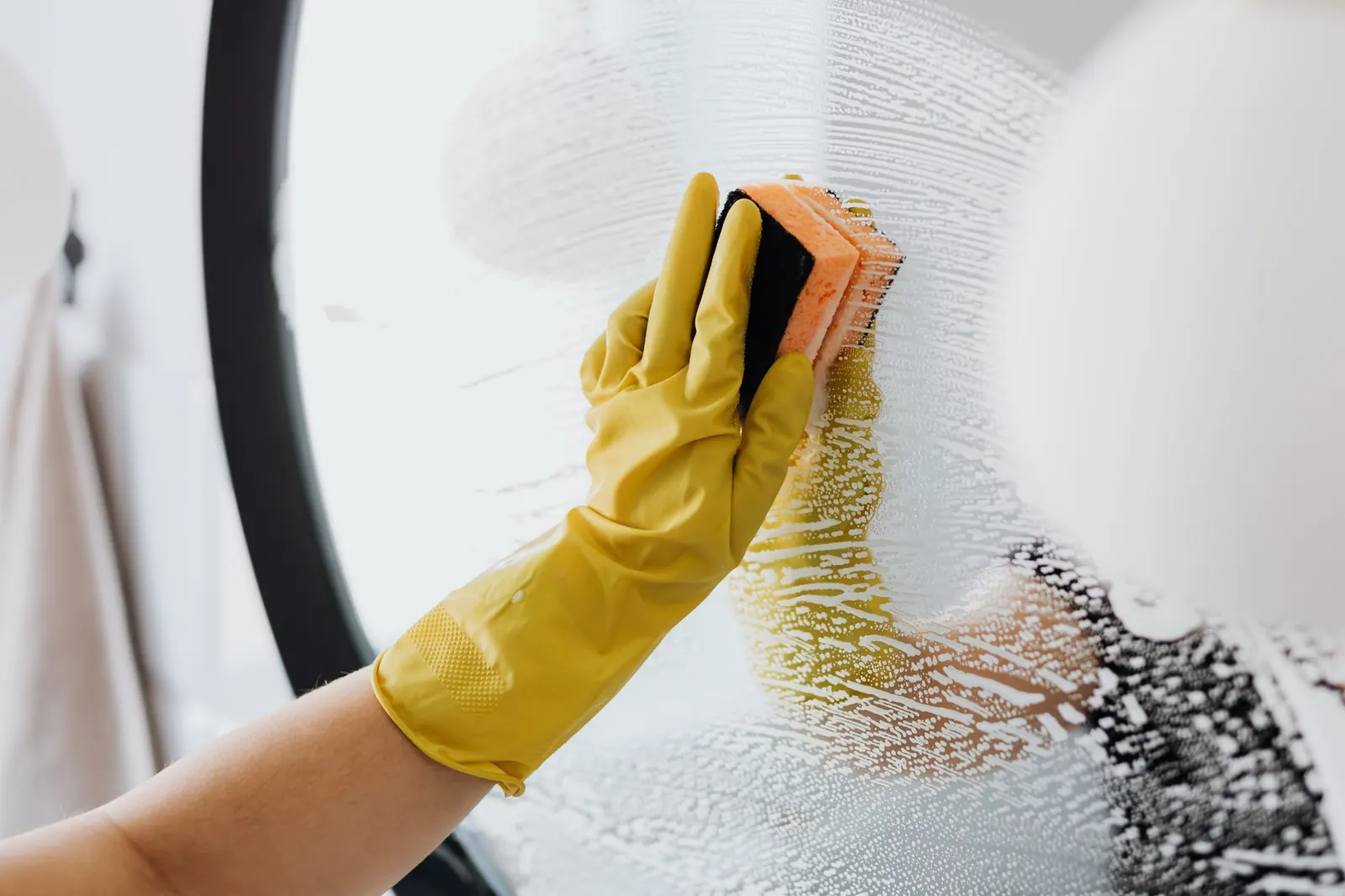 Gloved hand wiping a round mirror with a sponge